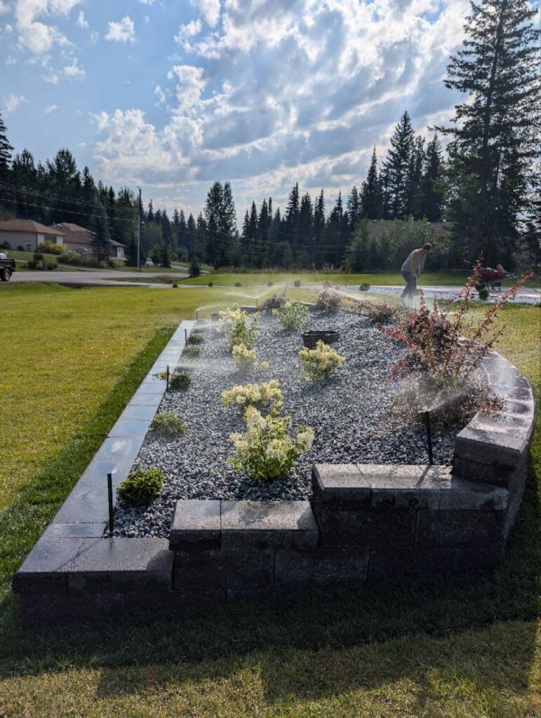 A newly installed garden bed featuring low-voltage lighting, mulching, and an active sprinkler irrigation system on a level property.