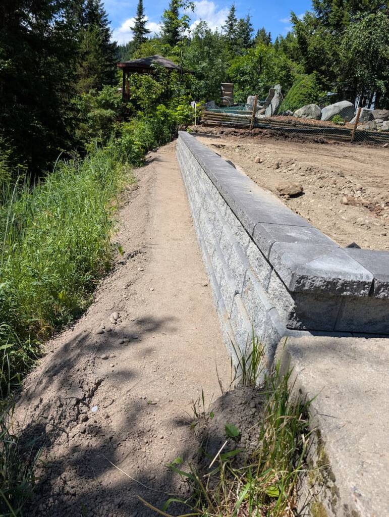 A long, clean structural retaining wall made of stacked grey blocks built to stabilize a significant slope on a large residential property.