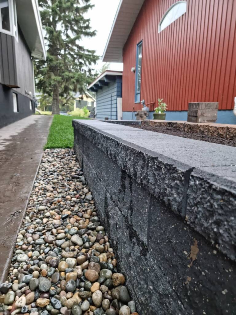 A crisp, modern grey retaining wall installation bordered by clean river rock and a walkway in Northern BC.